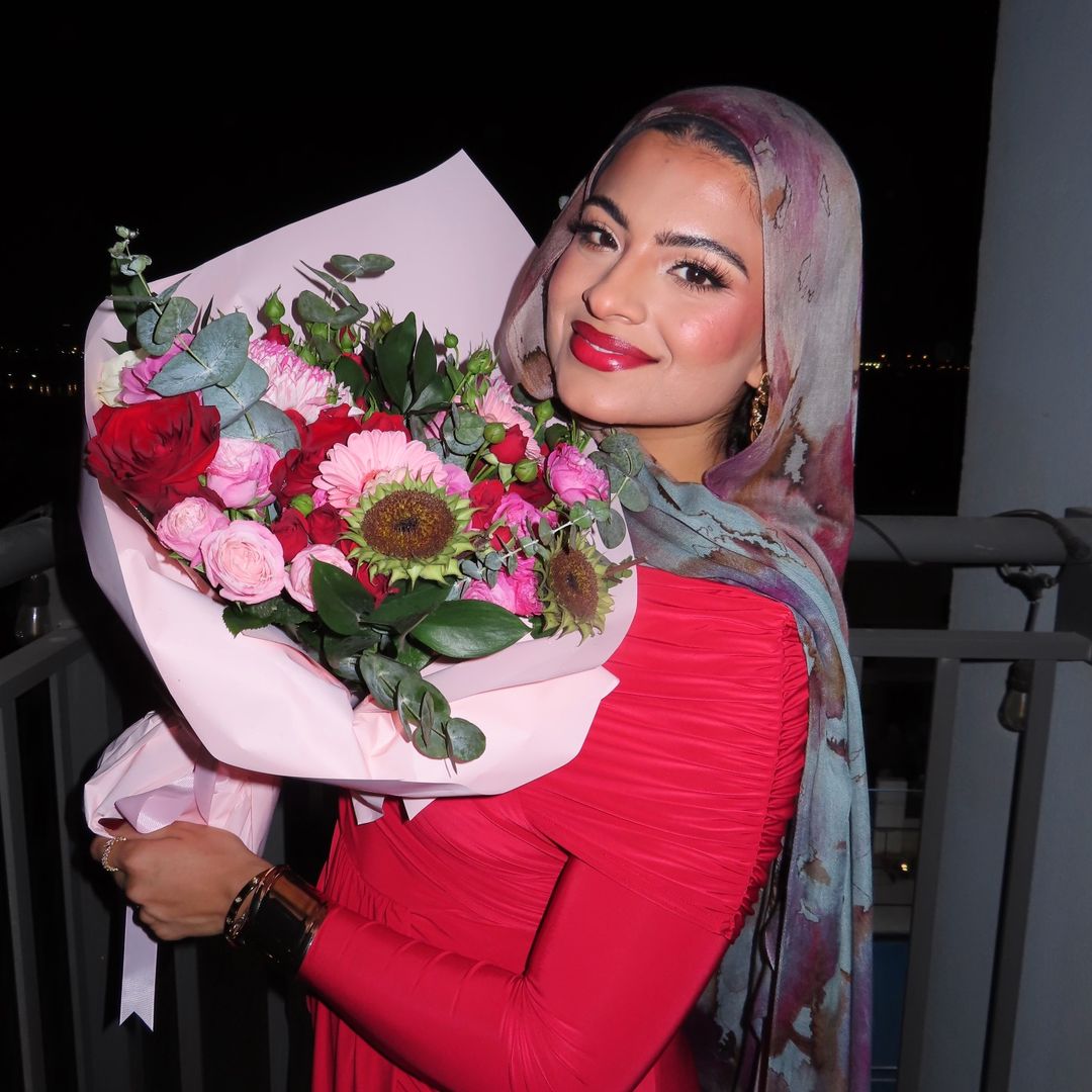 Aliya in a red dress holding a bouquet of roses against the night skyline